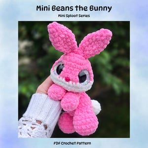 May include: A pink and white crocheted plush bunny toy with large, glittery black eyes and a small pink heart-shaped nose. The text above reads Mini Beans the Bunny, Mini Sploot Series, and the text below reads PDF Crochet Pattern.