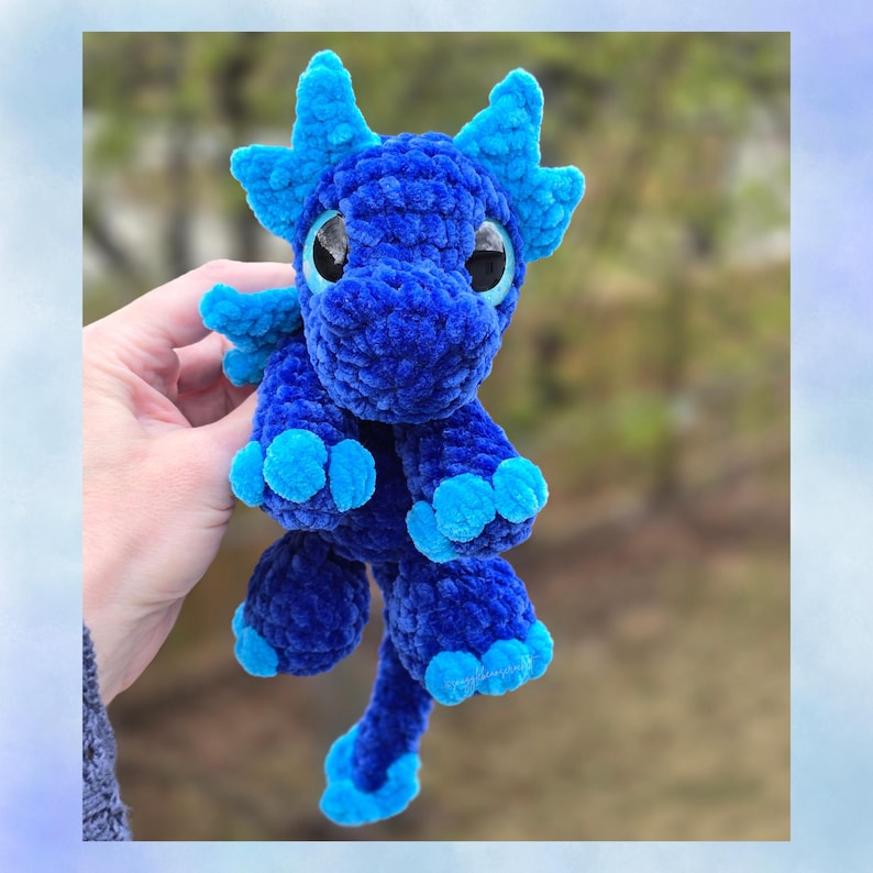 Puede incluir: Un drag&oacute;n azul hecho a mano con ganchillo, con detalles en azul claro en los cuernos, las alas y los pies. El peluche tiene ojos grandes y redondos y un aspecto suave y texturizado. El drag&oacute;n es un art&iacute;culo caprichoso de tem&aacute;tica fant&aacute;stica.