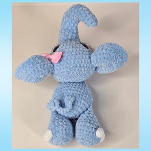 K&ouml;nnte beinhalten: Ein hellblaues geh&auml;keltes Elefanten-Pl&uuml;schtier mit R&uuml;ssel, gro&szlig;en Ohren und einer rosa Schleife. Der Elefant hat wei&szlig;e Akzente an den F&uuml;&szlig;en und einen eingerollten Schwanz. Das Spielzeug ist aus weichem, strukturiertem Garn gefertigt.