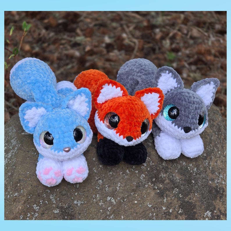 Puede incluir: Tres juguetes de peluche en azul, naranja y gris. El juguete azul tiene una gran cola esponjosa y patas rosas. El juguete naranja es un zorro con patas negras. El juguete gris tiene ojos azules brillantes. Todos tienen ojos grandes y brillantes.