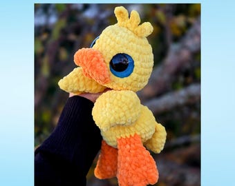 May include: A yellow crocheted duck plush toy with a textured yarn finish, large blue eyes, and bright orange feet and beak. The text at the top reads Dumpling the Duck Sploot Series, and the text at the bottom reads PDF Crochet Pattern.