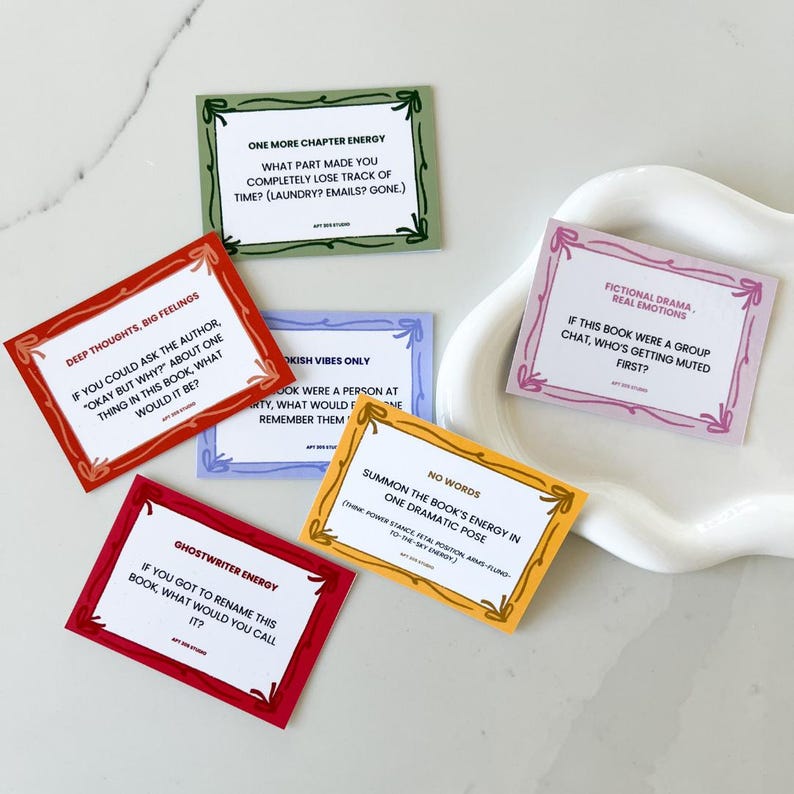 May include: A collection of colorful, square cards with text prompts for book lovers. Each card has a different color border and features phrases like "One More Chapter Energy" and "Ghostwriter Energy."