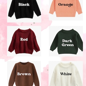 May include: Five different colored sweaters with the color name printed on each. The colors are black, orange, red, dark green, and white. The sweaters are all the same style, with a crew neck and long sleeves. The sweaters are all on a pink background with white polka dots.