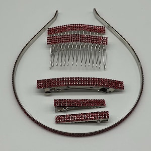 May include: A set of red rhinestone hair accessories, including a headband, hair comb, and several barrettes. The accessories have a silver metal base and are adorned with small, sparkling red rhinestones. The headband and barrettes are of varying sizes.