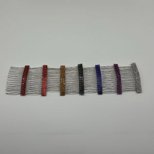 May include: A collection of seven hair combs with silver metal teeth. Each comb features a rectangular band adorned with sparkling rhinestones in various colors: red, pink, gold, black, blue, purple, and silver. These accessories are designed for hair styling.