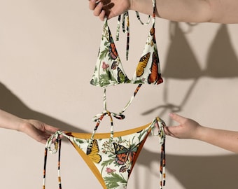 May include: A white bikini with a floral and butterfly print. The top is a triangle style with adjustable straps. The bottom is a cheeky style with ties on the sides.