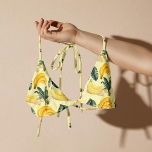May include: A yellow bikini top with a banana print. The top has adjustable straps and a tie closure at the back.