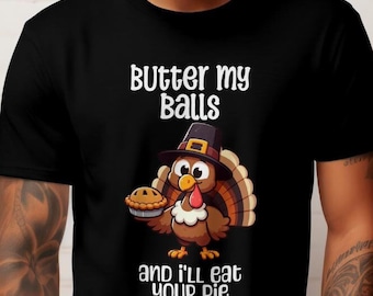 May include: Black t-shirt with a Thanksgiving-themed graphic. The graphic features a cartoon turkey wearing a pilgrim hat and holding a pie, with the text "Butter my Balls and I'll eat your pie."