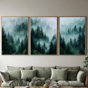 Puede incluir: Tres impresiones artísticas enmarcadas que representan una escena de bosque brumoso con altos árboles de hoja perenne. La obra de arte tiene un marco de madera natural y se exhibe sobre un sofá verde salvia con cojines a juego. Una mesa de centro de madera y plantas decorativas completan la habitación.