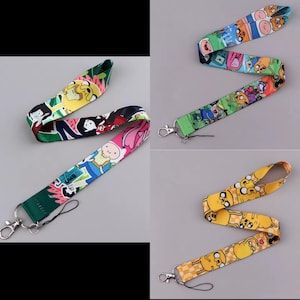 May include: Four colorful lanyards featuring cartoon characters. Designs include characters on green, blue, and yellow backgrounds. Each lanyard has a metal clasp and a black cord for attaching keys or an ID badge. The lanyards are on a gray background.