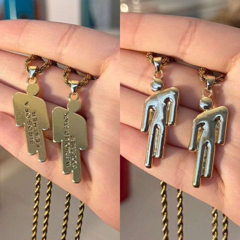 May include: Two gold-colored pendant necklaces. One pendant has the text "BIRDS OF A FEATHER" and the other says "WE SHOULD STICK TOGETHER". The other two pendants have a stylized human figure design. The necklaces have gold-colored rope chains.