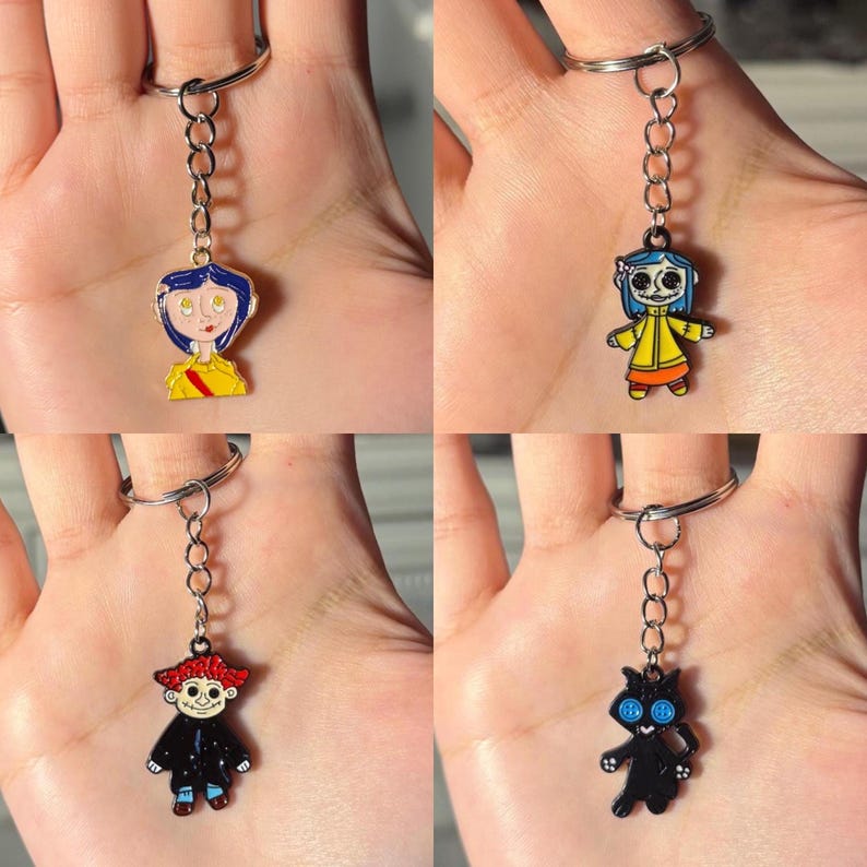 May include: Four keychains featuring characters from a movie. Each keychain has a silver ring and chain. The characters are depicted in enamel with bright colors. One character has blue hair and a yellow shirt. Another is a black cat with button eyes.