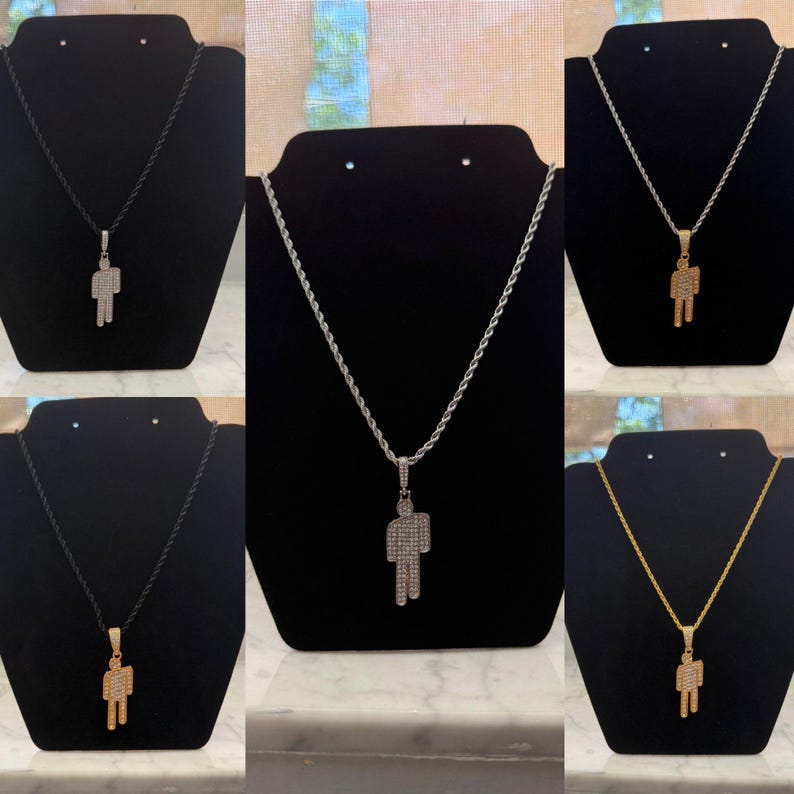 May include: A collection of necklaces featuring a pendant in the shape of a person. The pendants are encrusted with small, shiny stones. The necklaces are displayed on black stands, with different chain styles and colors.