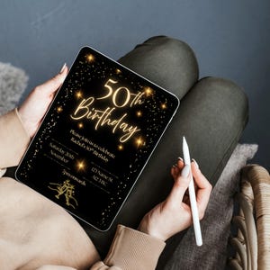 May include: A black digital tablet displays a gold-colored 50th birthday invitation. The invitation text includes "50th Birthday" in elegant script, along with event details. A white stylus rests beside the tablet, held by a person.