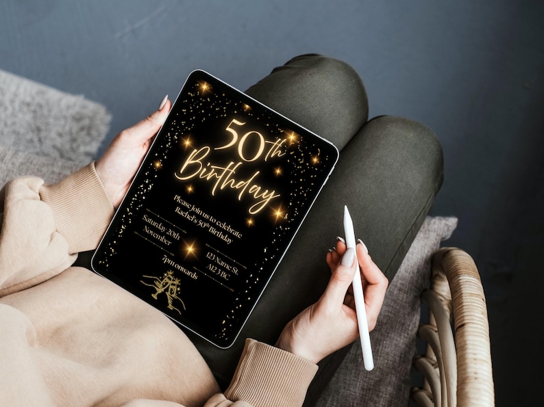 May include: A black digital tablet displays a gold-colored 50th birthday invitation. The invitation text includes "50th Birthday" in elegant script, along with event details. A white stylus rests beside the tablet, held by a person.