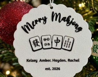 May include: A white scalloped circular ornament with a silver hanging string. The text reads Merry Mahjong above four mahjong tiles, followed by the names Kelsey, Amber, Hayden, Rachel, and the text est. 2026 in black ink.