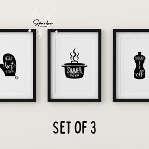 May include: Set of three black and white kitchen-themed prints in black frames. The prints feature a black oven mitt with the text "Hello hot stuff", a black pot with the text "Simmer down", and a black salt shaker with the text "Shake it off".