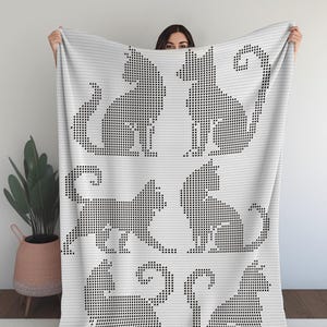 May include: White blanket featuring a repeating pattern of black cat silhouettes in various poses. The cats are created using a pixelated design, giving the blanket a modern, graphic look. The blanket is made of a soft, comfortable material.