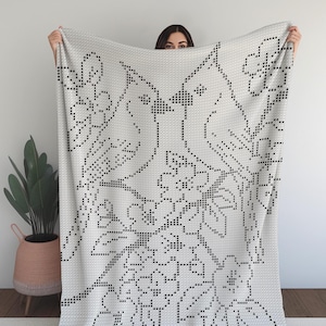 May include: A white blanket featuring a black floral and bird pattern. The design is made up of small, evenly spaced black dots, creating detailed images of flowers, leaves, and birds. The blanket is displayed, highlighting the full design.
