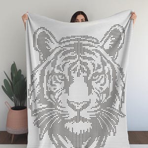 Może przedstawiać: Biały koc z czarnym wzorem twarzy tygrysa. Twarz tygrysa jest stworzona za pomocą wzoru kropek. Koc jest wykonany z miękkiego, tkanego materiału. Odpowiedni do sypialni lub salonu.