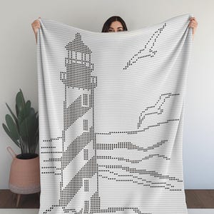 May include: White blanket featuring a black pixelated design of a lighthouse, waves, and a seagull. The lighthouse has black and white stripes. The blanket is held up by a person.