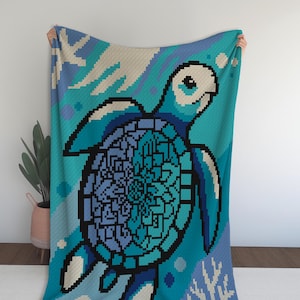 May include: A pixelated blanket featuring a sea turtle design in shades of blue, teal, and black. The turtle's shell has a detailed, geometric pattern. The background includes diagonal stripes and aquatic elements, creating a marine theme.