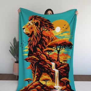 Könnte beinhalten: Eine türkisfarbene Decke mit einer pixeligen Illustration eines Löwen im Profil, vor einer afrikanischen Savannenlandschaft. Das Design umfasst einen Wasserfall, Bäume, einen Sonnenuntergang und Vögel. Der Löwe ist in Orange-, Braun- und Schwarztönen dargestellt.
