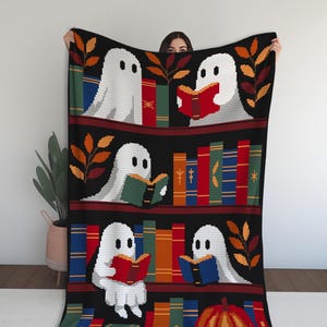 Könnte beinhalten: Eine schwarze gehäkelte Decke mit einem Bücherregal-Design. Weiße Geisterfiguren lesen Bücher in verschiedenen Farben. Es gibt orangefarbene und braune Blätterakzente. Unten befindet sich ein Kürbis.