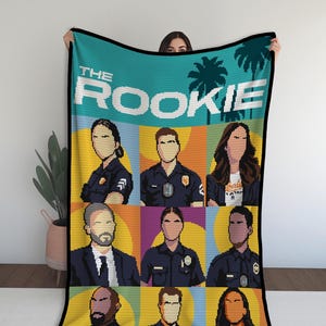 May include: A pixelated blanket featuring the text "THE ROOKIE" above nine character portraits. The blanket has a teal background with palm trees and a black border. The portraits are set against colorful geometric backgrounds.