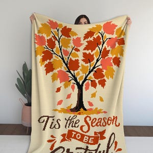 May include: Cream-colored throw blanket featuring a fall tree design with orange, yellow, and red leaves. The blanket has the text "Tis the Season to be Grateful" in brown script. A cozy autumn-themed home decor item.