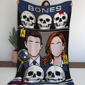 May include: A navy blue blanket featuring a pixelated design with the word "BONES" at the top. The design includes skulls, two faceless figures, a magnifying glass, and the letters "A" and "B" on yellow tags.