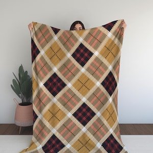 Op de afbeelding: Een groot plaid met een ruitpatroon in de kleuren bruin, rood en geel. De deken is gemaakt van een zachte, comfortabele stof en is perfect om te knuffelen op de bank.