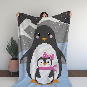 Peut inclure: Une couverture au crochet représentant un grand pingouin avec un petit pingouin devant lui. Les pingouins sont blancs avec des accents noirs et l'arrière-plan est une scène enneigée bleue et grise.