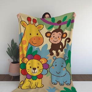 Op de afbeelding: Een gehaakte deken met een kleurrijke junglescène, met een giraffe, aap, leeuw en nijlpaard. De deken heeft een beige achtergrond met blauwe en groene bladeren. De dieren zijn in heldere kleuren, geschikt voor een kinderkamer.