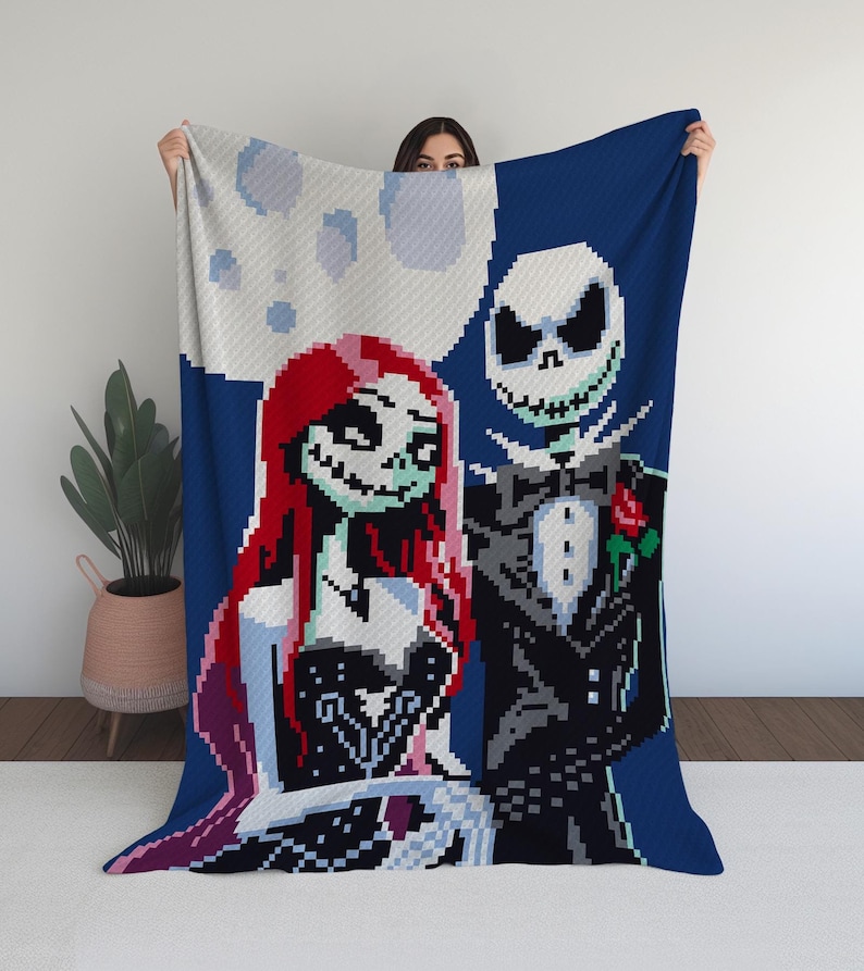 Puede incluir: Una manta de punto azul, blanca y roja con una imagen pixelada de Jack Skellington y Sally de la pel&iacute;cula Pesadilla antes de Navidad. Los personajes est&aacute;n de pie juntos, con Jack con un esmoquin negro y Sally con un vestido negro.