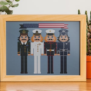 May include: A framed cross-stitch design featuring five figures in military uniforms. The figures are standing in a row, with an American flag above them. The text "United We Stand" is printed below the figures.