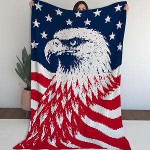 May include: A rectangular knit blanket featuring a pixelated graphic of a bald eagle head in white and dark blue, set against a background of a stylized American flag with red and white horizontal stripes and white stars on a dark blue field.