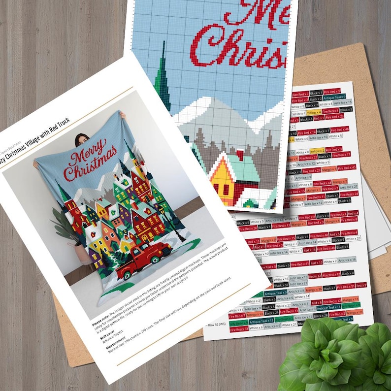 May include: A light blue blanket with a Christmas village design, featuring colorful houses, a red truck, and the text "Merry Christmas." Accompanying the blanket are pattern instructions and a chart for a cross-stitch project.
