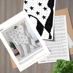 Pu&ograve; includere: Una coperta all'uncinetto con un disegno che ricorda la bandiera americana, con stelle e strisce. La coperta &egrave; tenuta in mano, mostrando il motivo. Le istruzioni e una tabella accompagnano la coperta.