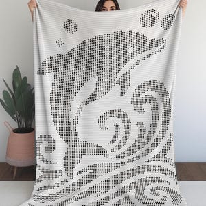 May include: White blanket with a black pixelated dolphin design leaping over waves. The blanket has a textured appearance and is held up against a white background. The design includes bubbles and a star.