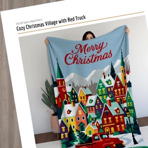 May include: A crocheted Christmas blanket featuring a village scene with colorful houses, snow-covered ground, and a red truck. The blanket has a light blue background with the words "Merry Christmas" in red. The text "Cozy Christmas Village with Red Truck" is also visible.