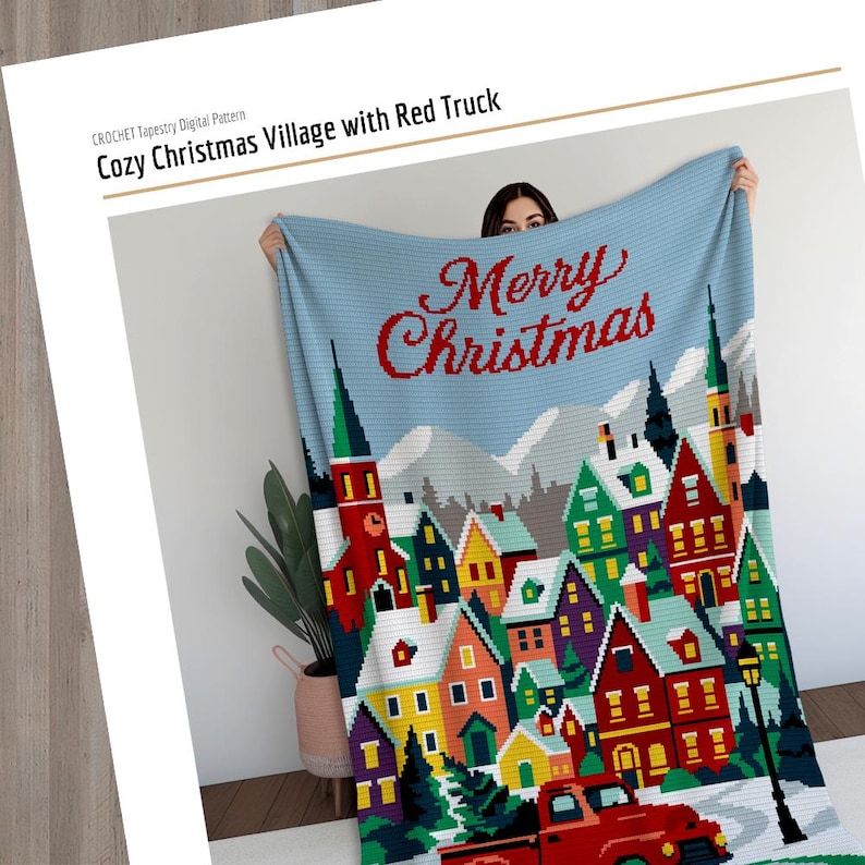 May include: A crocheted Christmas blanket featuring a village scene with colorful houses, snow-covered ground, and a red truck. The blanket has a light blue background with the words "Merry Christmas" in red. The text "Cozy Christmas Village with Red Truck" is also visible.