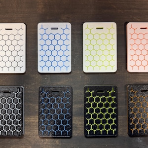 May include: Eight rectangular ID badge holders with a honeycomb pattern. The top row features white, blue, yellow-green, and coral holders. The bottom row includes black, blue, yellow-green, and orange holders. Each has a slot for a lanyard.