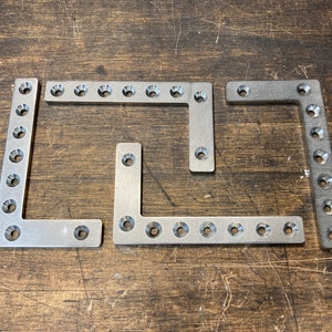 May include: Four silver metal corner brackets with multiple holes for screws. The brackets are arranged in a L shape.