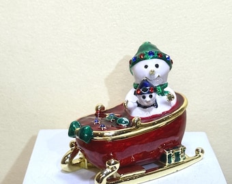 A loving snowman dad cuddles his baby in a sparkling sleigh. Hand-painted enamel, festive colors—ideal for Christmas displays and meaningful