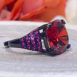 May include: A black ring with a large red gemstone and a band accented with small pink gemstones.