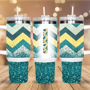 May include: Three stainless steel tumblers with a teal and yellow chevron pattern and glitter accents. The center tumbler has the word "Grandma" printed on it.