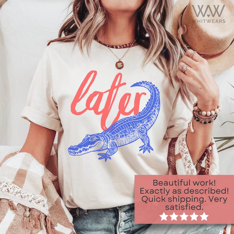 May include: A white t-shirt with a blue alligator and the word "later" in red. The alligator is facing left and has a detailed design.