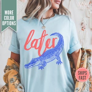 May include: Light blue t-shirt with a blue alligator and the word "later" in red.