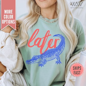 May include: A light blue t-shirt with a blue and white alligator graphic and the word "later" in red lettering.